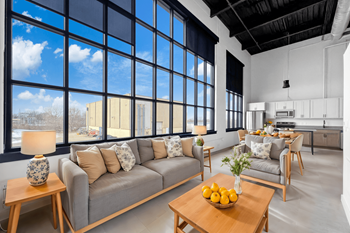 A modern living room with a grey sofa, wooden coffee table, and a large window.at Plant 1 Lofts, N. Newton, IA  